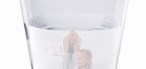 Two blurred figures, one adult and one child, are visible through a glass of water.