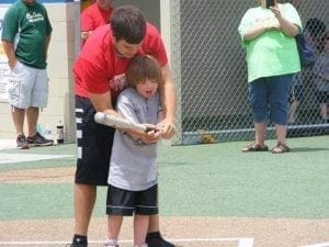 A young boy with his arm around a baseball bat held by a man.
