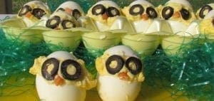 Deviled eggs decorated to look like chicks with olive eyes and carrot beaks