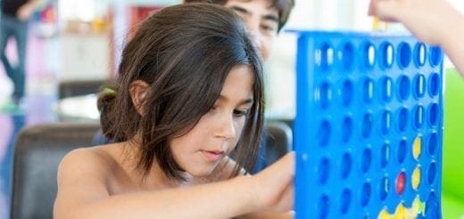 A young girl plays Connect Four with two other children.