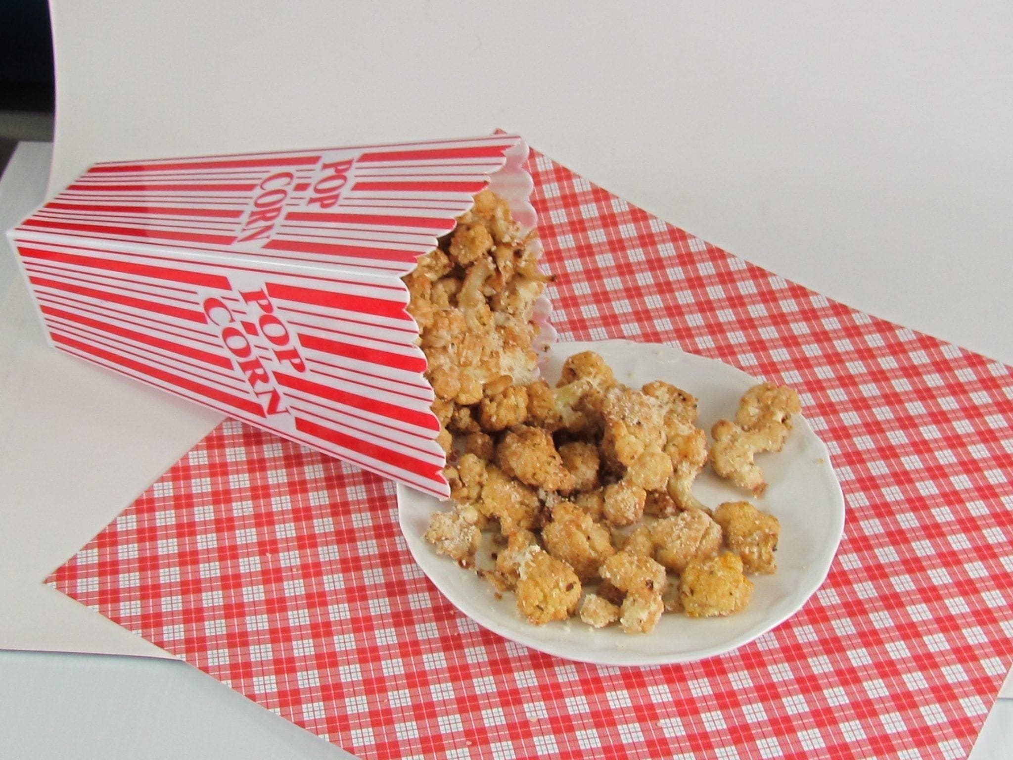 Cauliflower popcorn spilling from a red and white striped box onto a white plate.