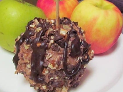 Caramel apple drizzled with chocolate and nuts, with whole apples in the background