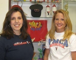 Kristy McKinney and Jessica Collins stand before a YMCA display, representing the Special Needs Summer Program organizers.