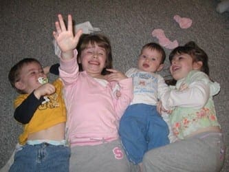 Four young children laughing and playing together while lying on a carpeted floor.