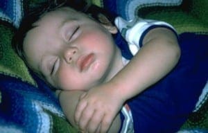Young baby sleeping peacefully on a colorful textured blanket.