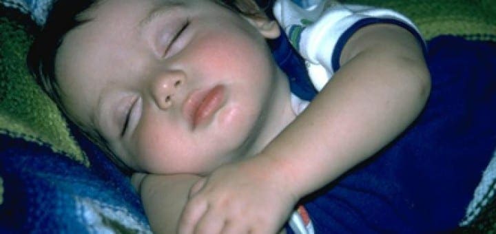 Young baby sleeping peacefully on a colorful textured blanket.