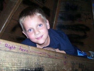 Seven-year-old Kaden looks toward the camera with a gentle smile while resting on a wooden structure.