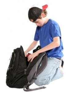 Student kneeling on the floor to organize school supplies and papers inside a backpack.