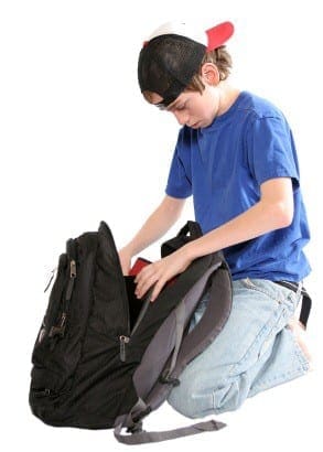Student kneeling on the floor to organize school supplies and papers inside a backpack.