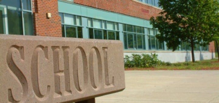 Stone sign reading School in front of a modern brick school building.