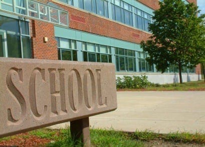 Stone sign reading School in front of a modern brick school building.