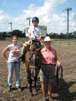Child in a riding helmet sits on a horse accompanied by two women at the Okeechobee Special Equestrian Therapeutic Center.