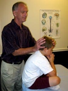 Practitioner performing gentle cranial sacral therapy on a child in a clinical setting.