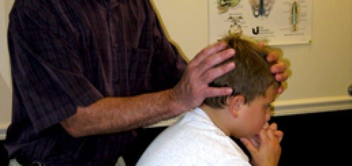 Practitioner performing gentle cranial sacral therapy on a child in a clinical setting.