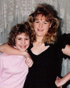 Two smiling sisters with curly hair embracing warmly in a family portrait.