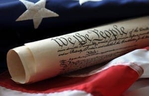 Parchment document featuring the text We the People resting against an American flag.