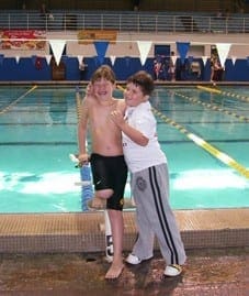 Evan and a friend smile and pose together on the edge of the Treasure Coast Swimming pool.