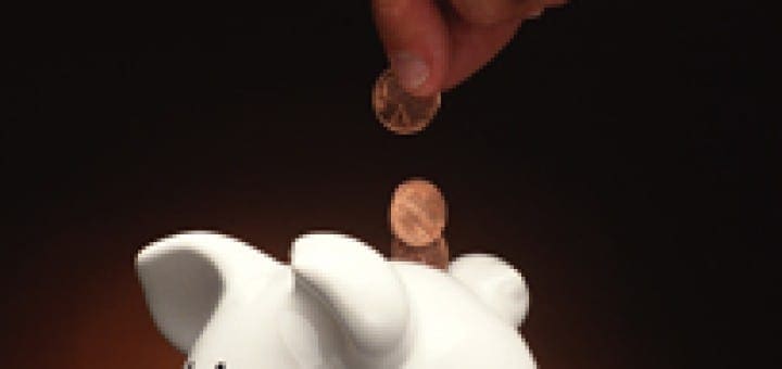 Hand placing a coin into a white piggy bank to teach children the importance of saving money.