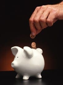 Hand placing a coin into a white piggy bank to teach children the importance of saving money.