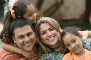 Smiling parents embracing their two young daughters, illustrating a connected and positive family unit.