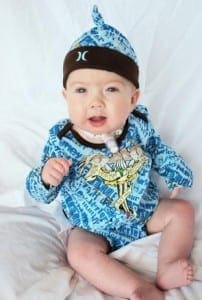 Infant Jayson wearing a blue printed onesie and beanie while receiving care in the NICU.