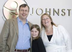 A man, a woman, and a girl smile in front of a wall with "JOHNSTON" on it.