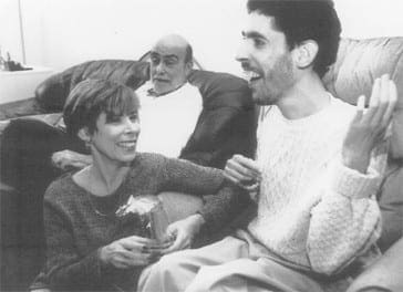 Jeremy sits on a sofa with his mother and another man, smiling and gesturing while engaged in a conversation.