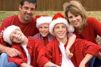 Smiling family of four wearing matching red shirts and Santa hats celebrate the holidays together.