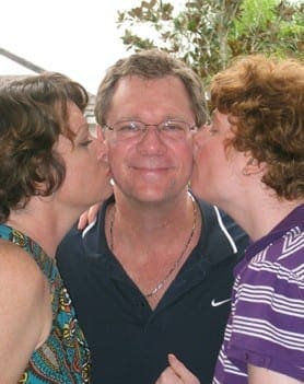 Two women kiss a man on the cheeks.