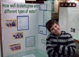 Evan proudly poses next to his science fair project about plants and water.