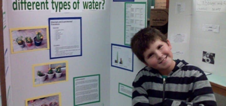Evan proudly poses next to his science fair project about plants and water.