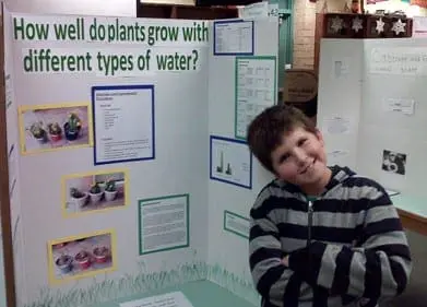 Evan proudly poses next to his science fair project about plants and water.