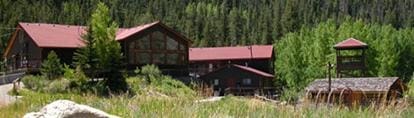 Buildings with red roofs are nestled against a forest and tall grasses.