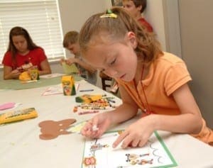 Children work on crafts at a table with art supplies and paper cutouts.