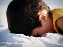 Boy with head down in the sand, focusing on the details.