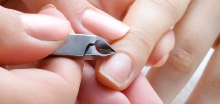 Hands trim nails with cuticle nippers.