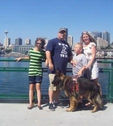 A family of four and their service dog pose for a picture with a city skyline in the background.