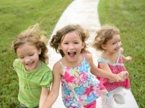 Three young girls joyfully run down a winding path on a sunny day.