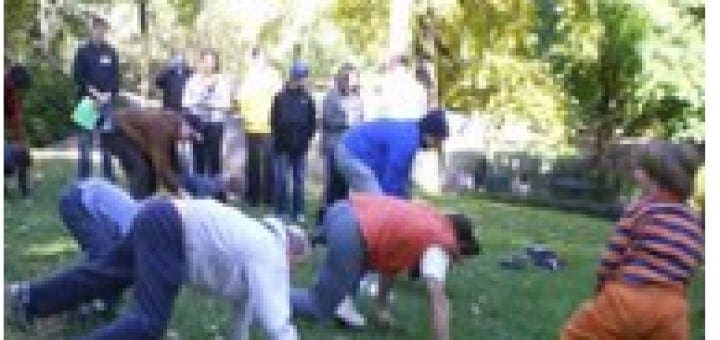 People in a park exercise class practice crawling on grass while a child watches.