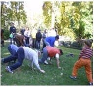 People in a park exercise class practice crawling on grass while a child watches.