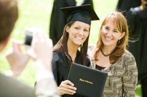 A graduate smiles with her proud mother as a person in the foreground takes a photo.