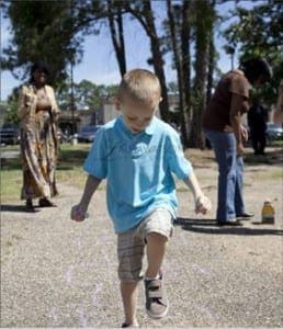 A young boy hops forward on one foot while two adults stand in the background.