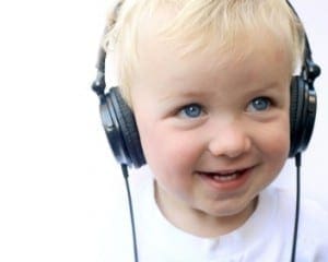 Blond haired boy with blue eyes wearing large headphones and smiling.