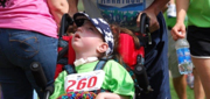 Man pushes girl in wheelchair with race bib number 260 at an outdoor event.
