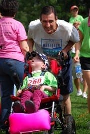 Man pushes girl in wheelchair with race bib number 260 at an outdoor event.