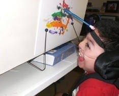 Child with a headband and assistive device paints a colorful abstract picture.