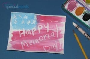 Child's drawing of a flag with "Happy Memorial Day!" written in white crayon, next to art supplies.
