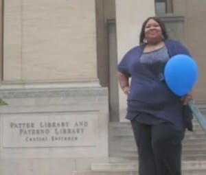 Shounda Hathaway smiles, holding a blue balloon in front of the Paterno Library at Penn State.