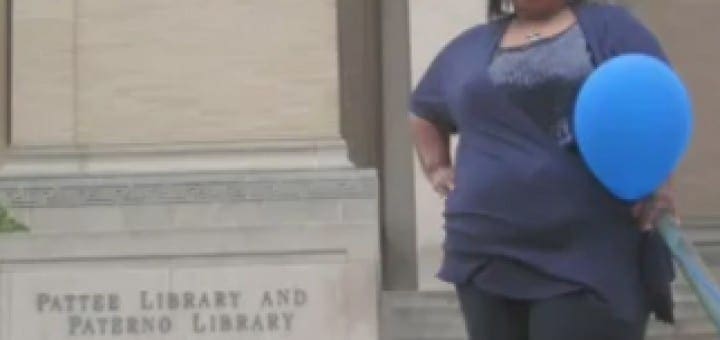 Shounda Hathaway smiles, holding a blue balloon in front of the Paterno Library at Penn State.