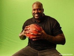 Shaquille O'Neal holds a basketball against a green background.